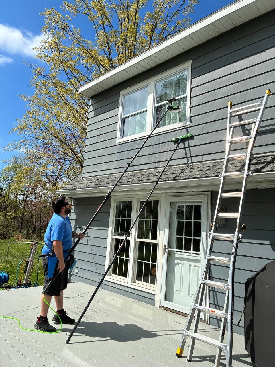 Water fed pole reaching upper-story window on Grand Rapids home — cleaner stands safely on deck